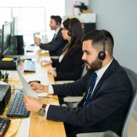 Side view of a latin man with a headset reading instructions and holding some paperwork. Sales representative working on telemarketing and customer service